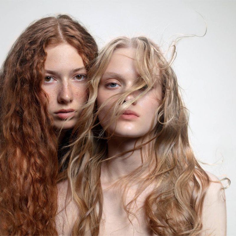 Blonde and redhead women looking at camera, representing different hair types for a hair care routine